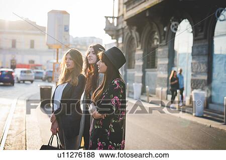 Three young women waiting on city street View Large Photo Image Stock Photo - Three young women waiting on city street. Fotosearch