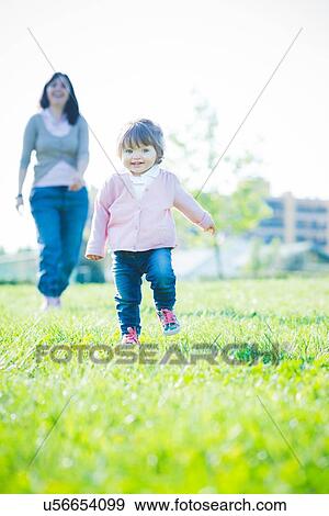 Stock Photo - Toddling female toddler in front of mother in park. Fotosearch