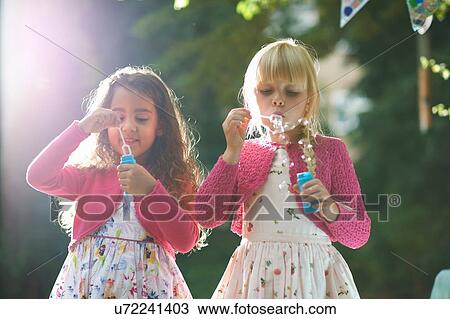 Stock Image - Two cute girls blowing bubbles in garden. Fotosearch