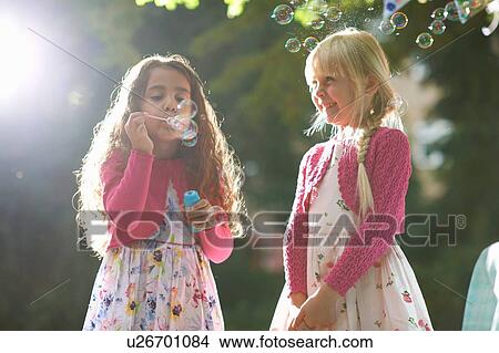 Two cute girls blowing bubbles in sunlit garden View Large Photo Image Picture - Two cute girls blowing bubbles in sunlit garden. Fotosearch