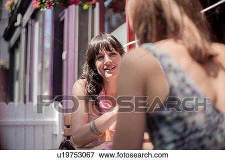 Stock Photo - Two female adult friends chatting whilst sitting outside pub. Fotosearch