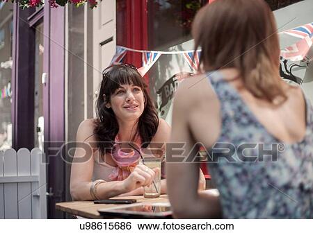 Two female adult friends chatting whilst sitting outside traditional pub View Large Photo Image Stock Photograph - Two female adult friends chatting whilst sitting outside traditional pub. Fotosearch