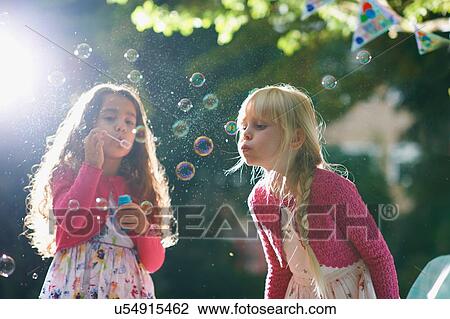 Stock Image - Two girls blowing bubbles in sunlit garden. Fotosearch