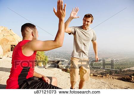 Stock Image - Two male friends, on top of mountain, giving high five. Fotosearch