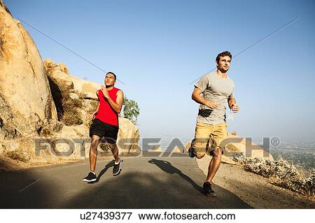 Stock Photo - Two male friends running along mountain path. Fotosearch
