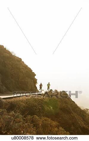 Stock Photo - Two male friends running along mountain path, rear view. Fotosearch