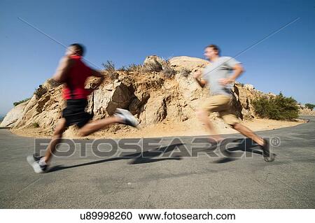 Stock Image - Two male friends, running, outdoors. Fotosearch