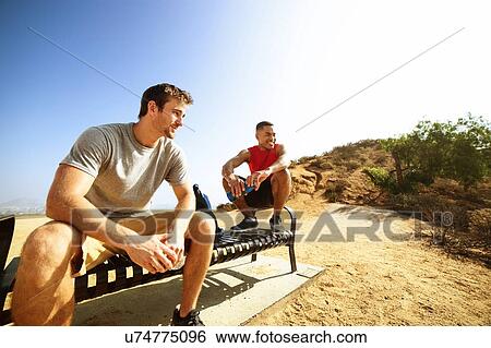 Two male friends, sitting on bench, on cliff top, looking at view View Large Photo Image Stock Photograph - Two male friends, sitting on bench, on cliff top, looking at view. Fotosearch