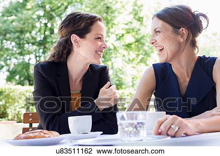 Stock Image - Two mature female friends chatting over coffee in garden. Fotosearch