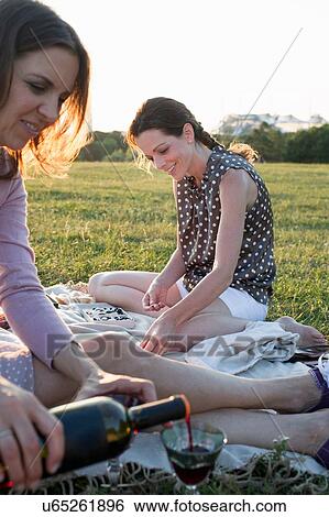 Stock Photograph - Two mature female friends pouring red wine in park. Fotosearch
