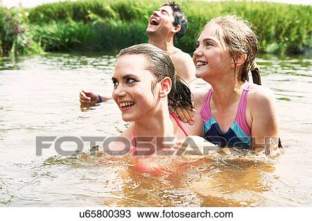 Stock Image - Two sisters and friend swimming in rural lake. Fotosearch