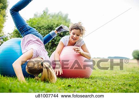 Picture - Two tween girls fooling around on exercise balls in garden. Fotosearch