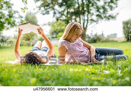 Stock Image - Two tween girls reading and using digital tablet in garden. Fotosearch