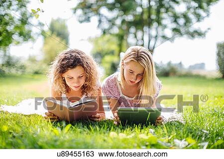 Two tween girls reading and using digital tablet whilst relaxing in garden View Large Photo Image Stock Image - Two tween girls reading and using digital tablet whilst relaxing in garden. Fotosearch