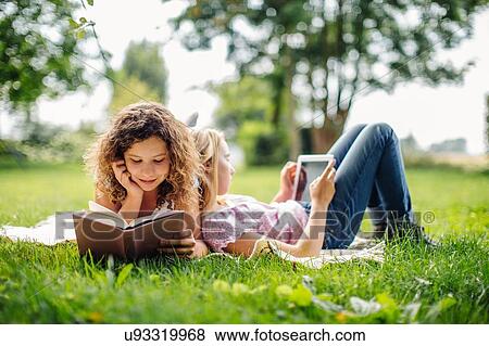 Two tween girls reading and using digital tablet whilst reclining in garden View Large Photo Image Stock Photo - Two tween girls reading and using digital tablet whilst reclining in garden. Fotosearch