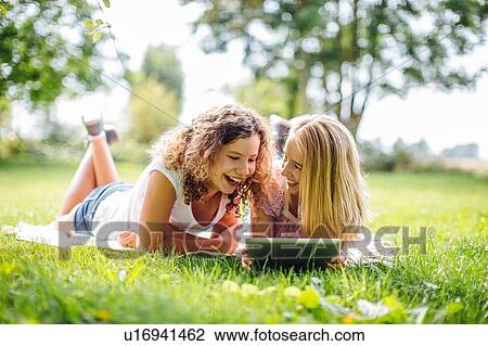 Stock Image - Two tween girls relaxing and browsing digital tablet in garden. Fotosearch