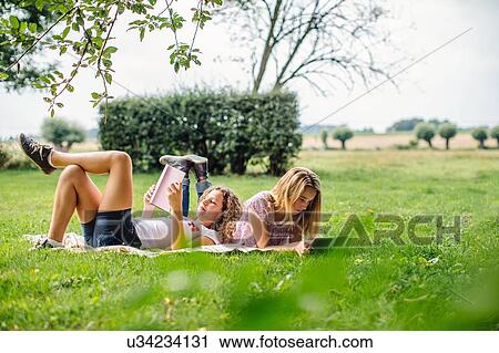 Two tween girls relaxing in garden reading and using digital tablet View Large Photo Image Stock Image - Two tween girls relaxing in garden reading and using digital tablet. Fotosearch