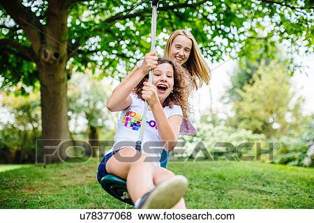 Two tween girls swinging on garden rope swing View Large Photo Image Stock Photo - Two tween girls swinging on garden rope swing. Fotosearch