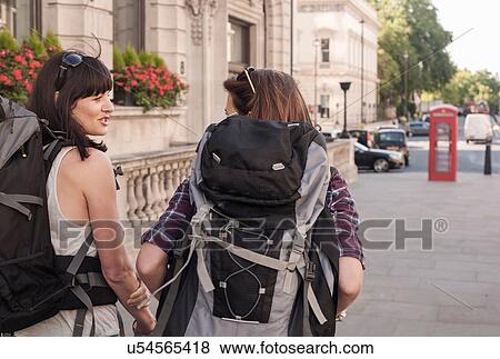 Stock Photo - Two women backpackers chatting whilst strolling on city sidewalk. Fotosearch