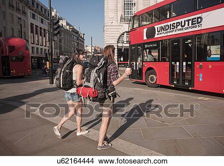 Picture - Two women backpackers crossing city road with takeaway coffee. Fotosearch