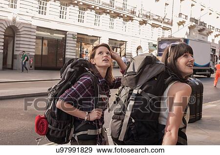 Stock Photo - Two women backpackers looking over their shoulders from city sidewalk. Fotosearch