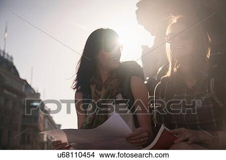 Picture - Two women backpackers sitting in sunlight city with map and guidebook. Fotosearch
