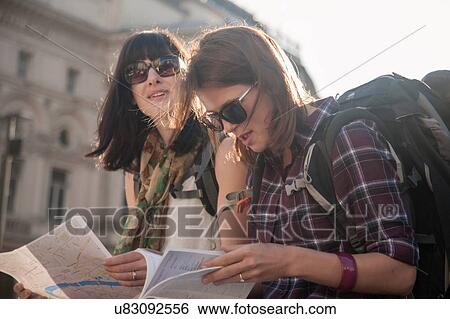 Stock Photograph - Two women backpackers sitting in sunlight reading map and guidebook. Fotosearch
