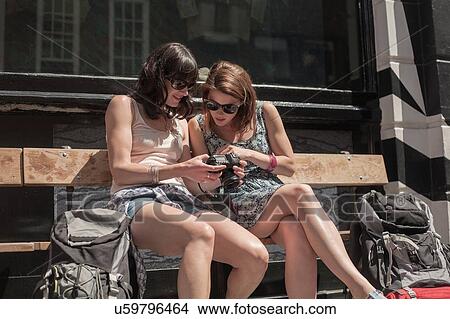 Two women backpackers sitting on bench reviewing camera photographs View Large Photo Image Picture - Two women backpackers sitting on bench reviewing camera photographs. Fotosearch