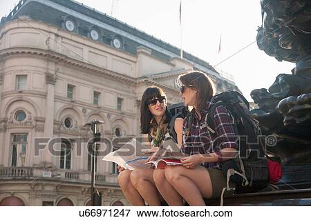 Two women backpackers sitting on statue steps with map and guide book, Picadilly Circus, London, UK View Large Photo Image Stock Photo - Two women backpackers sitting on statue steps with map and guide book, Picadilly Circus, London, UK. Fotosearch