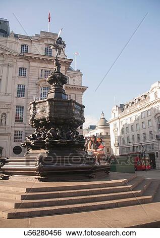 Stock Photograph - Two women backpackers sitting on statue steps, Picadilly Circus, London, UK. Fotosearch