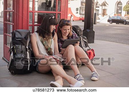 Two women backpackers sitting on sidewalk planning route on digital tablet, London, UK View Large Photo Image Stock Image - Two women backpackers sitting on sidewalk planning route on digital tablet, London, UK. Fotosearch