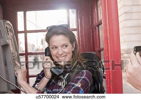 Picture - Two women backpackers taking smartphone photgraph in red telephone box, London, UK. Fotosearch