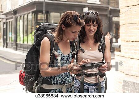 Two women backpackers using digital tablet to plan route from city street View Large Photo Image Picture - Two women backpackers using digital tablet to plan route from city street. Fotosearch