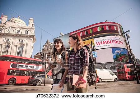 Stock Image - Two women backpackers with takeaway coffee, Picadilly Circus, London, UK. Fotosearch