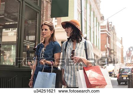 Two women carrying shopping bags looking at shop window View Large Photo Image Stock Image - Two women carrying shopping bags looking at shop window. Fotosearch