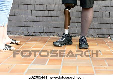 Stock Image - Two women standing together, mid adult woman wearing prosthetic leg, low section. Fotosearch
