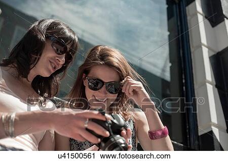 Stock Image - Two women wearing sunglasses reviewing camera photographs on city street. Fotosearch
