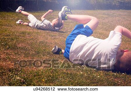 Stock Image - Two young brothers rolling on sunlit lawn. Fotosearch