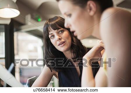 Two young brunette women sitting in a cafe talking having a business meeting View Large Photo Image Picture - Two young brunette women sitting in a cafe talking having a business meeting. Fotosearch
