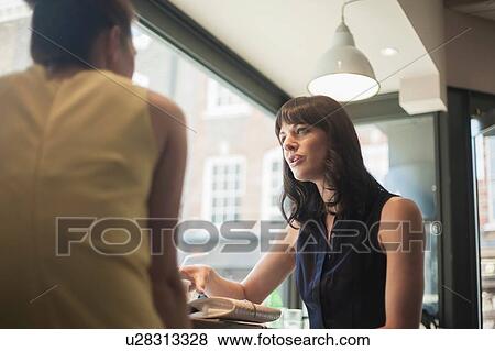Two young brunette women sitting in a cafe talking having a business meeting View Large Photo Image Stock Photo - Two young brunette women sitting in a cafe talking having a business meeting. Fotosearch