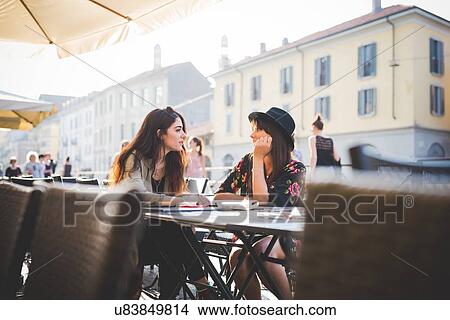 Picture - Two young women chatting at sidewalk cafe. Fotosearch