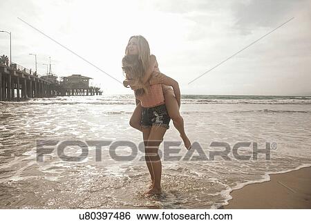 Two young women playing piggy backs in sea, Santa Monica, California, USA View Large Photo Image Stock Photograph - Two young women playing piggy backs in sea, Santa Monica, California, USA. Fotosearch