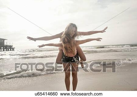 Two young women playing piggy backs with arms open on beach View Large Photo Image Stock Image - Two young women playing piggy backs with arms open on beach. Fotosearch