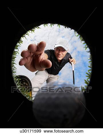 Stock Photo - View through hole of golfer reaching for golf ball. Fotosearch