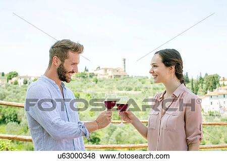 Stock Photo - Waist up side view of young couple face to face making a toast smiling. Fotosearch