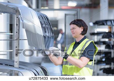 Stock Image - Worker checking paint finish on automotive parts in spray paint factory. Fotosearch