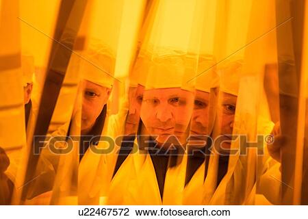 Stock Image - Worker inspecting circuit board under photographically safe light in circuit board factory, close up. Fotosearch