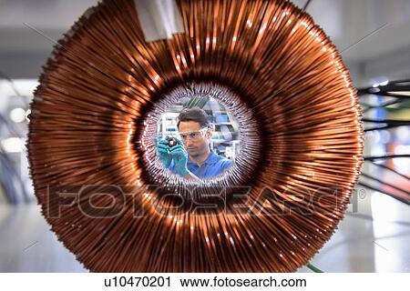 Worker inspecting electromagnetic coil seen through large coil in electromagnetics factory View Large Photo Image Stock Image - Worker inspecting electromagnetic coil seen through large coil in electromagnetics factory. Fotosearch