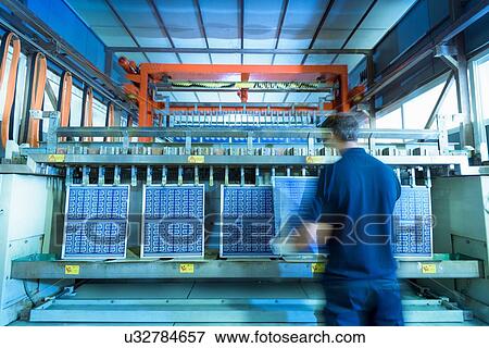 Stock Photo - Worker loading circuit boards into processing machine in circuit board factory. Fotosearch