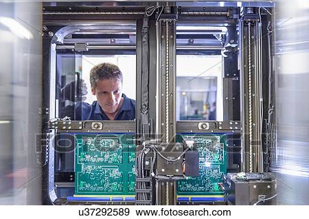 Stock Photo - Worker loading circuit boards into testing machine in circuit board factory. Fotosearch
